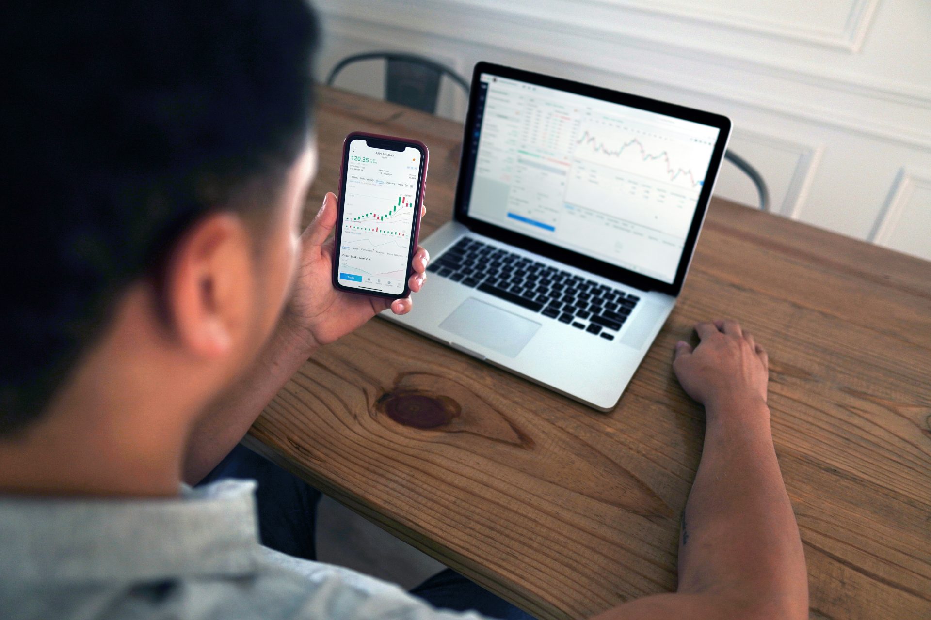 Person, die Börsentrends auf einem Smartphone mit Laptop-Hintergrund analysiert