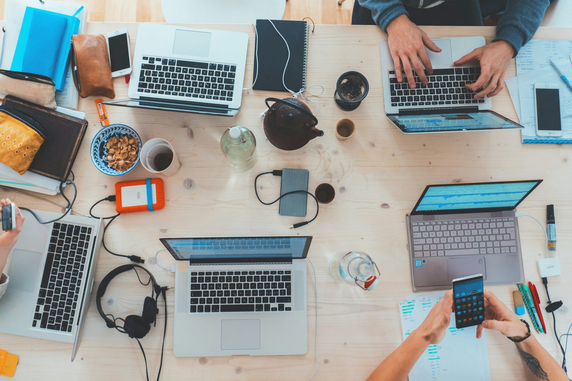 Menschen sitzen am Tisch mit verschiedenen Laptops